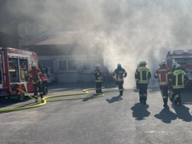 Feuerwehrübung, zwei Feuerwehrautos und einige Einsatzkräfte vor einem verrauchten Gebäude